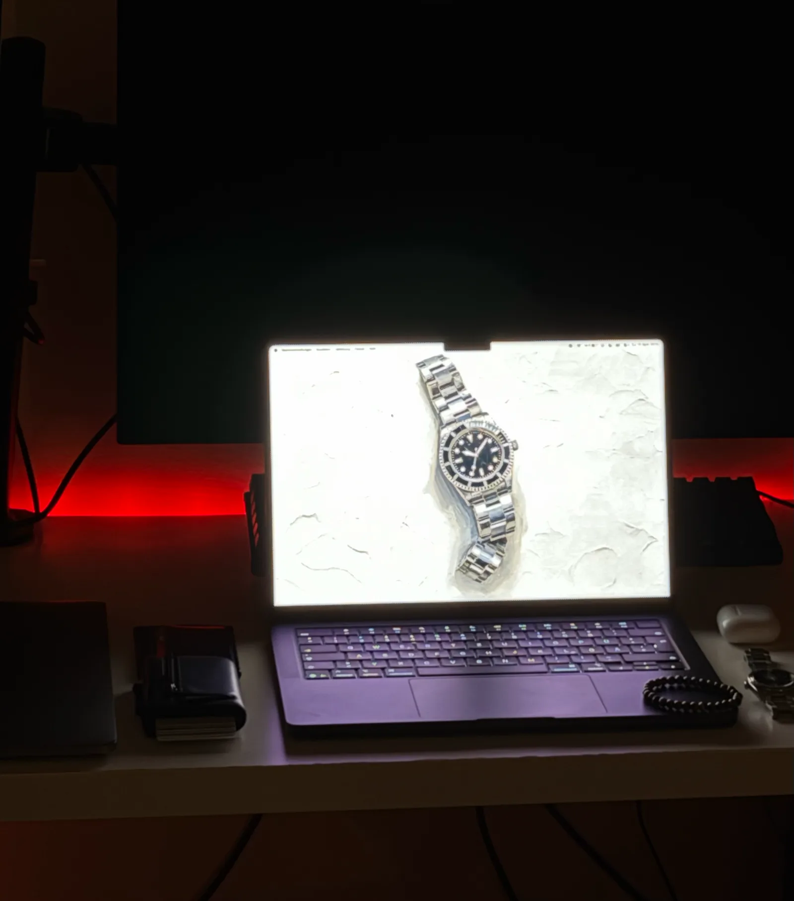 Arbeitsplatz mit rotem Lichtband hinter dem Tisch, auf dem Bildschirm die stählerne Taucheruhr.